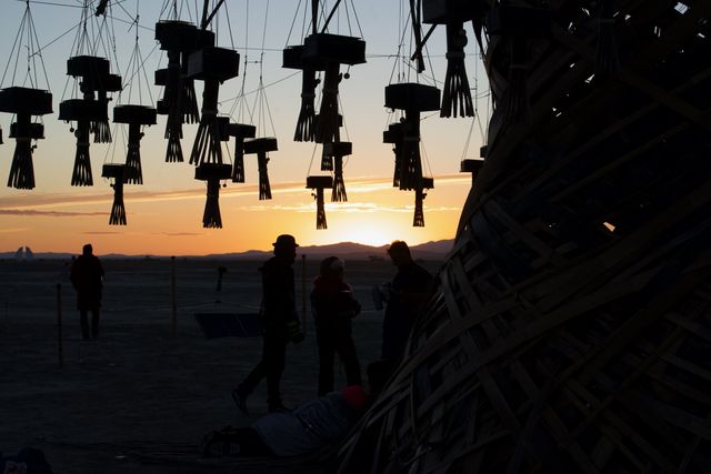 Sun on the horizon under the lanterns, silhouettes at the base.